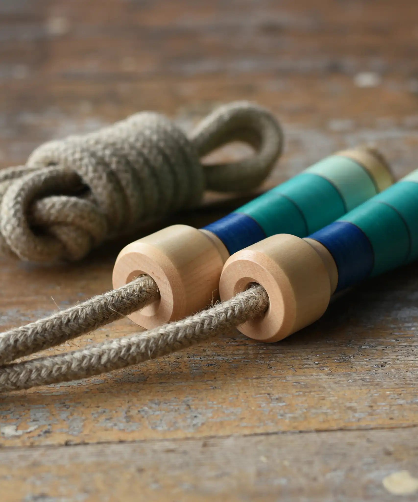 Mader Kreiselmanufaktur Skipping Rope with blue striped wooden handles placed on a wooden surface in the Babipur playroom. 