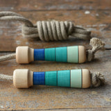 Mader Kreiselmanufaktur Skipping Rope with blue striped wooden handles placed on a wooden surface in the Babipur playroom. 