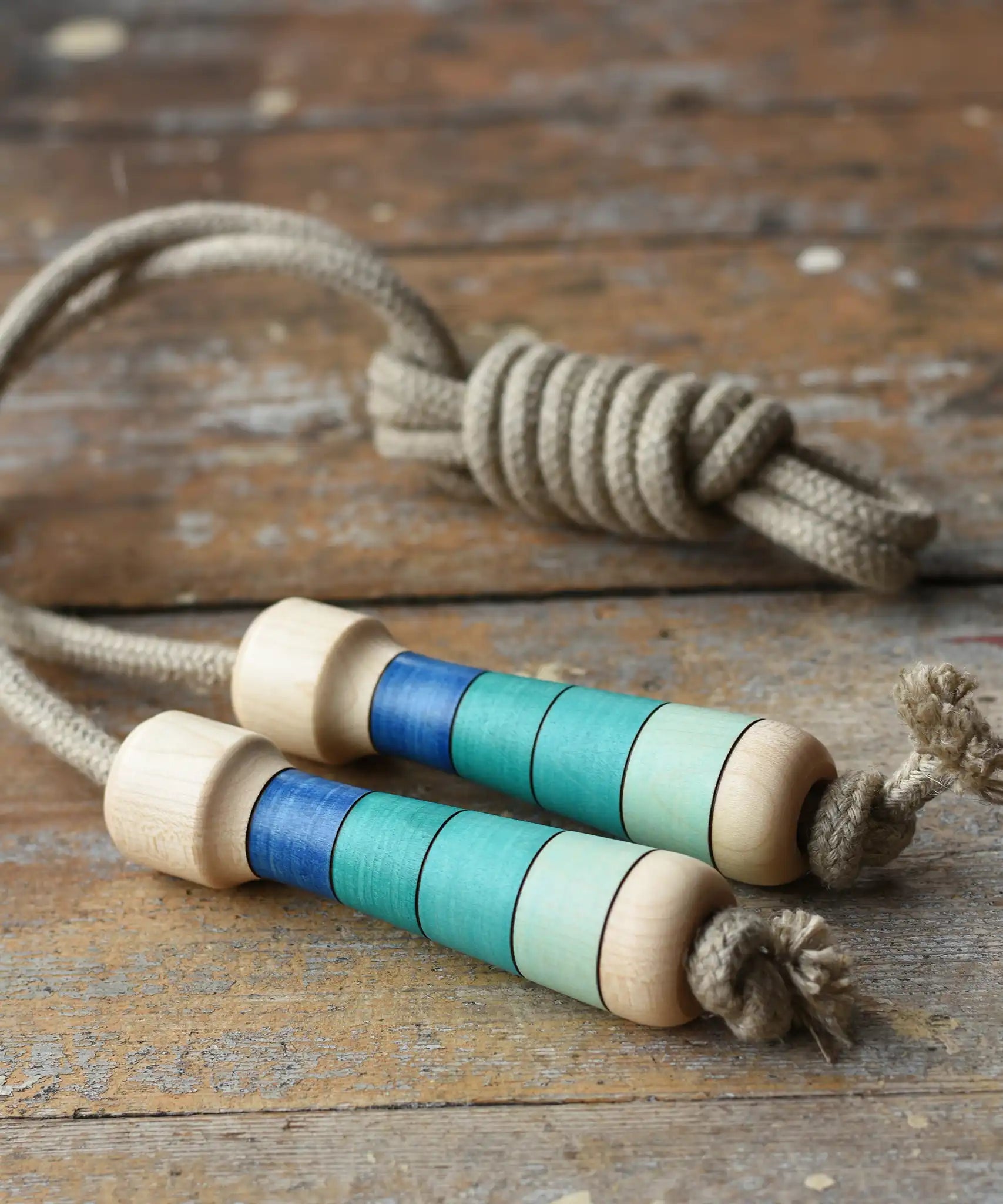 Mader Kreiselmanufaktur Skipping Rope with blue striped wooden handles placed on a wooden surface in the Babipur playroom. 