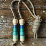 Mader Kreiselmanufaktur Skipping Rope with blue striped wooden handles placed on a wooden surface in the Babipur playroom. 