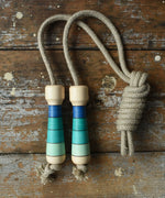 Mader Kreiselmanufaktur Skipping Rope with blue striped wooden handles placed on a wooden surface in the Babipur playroom. 
