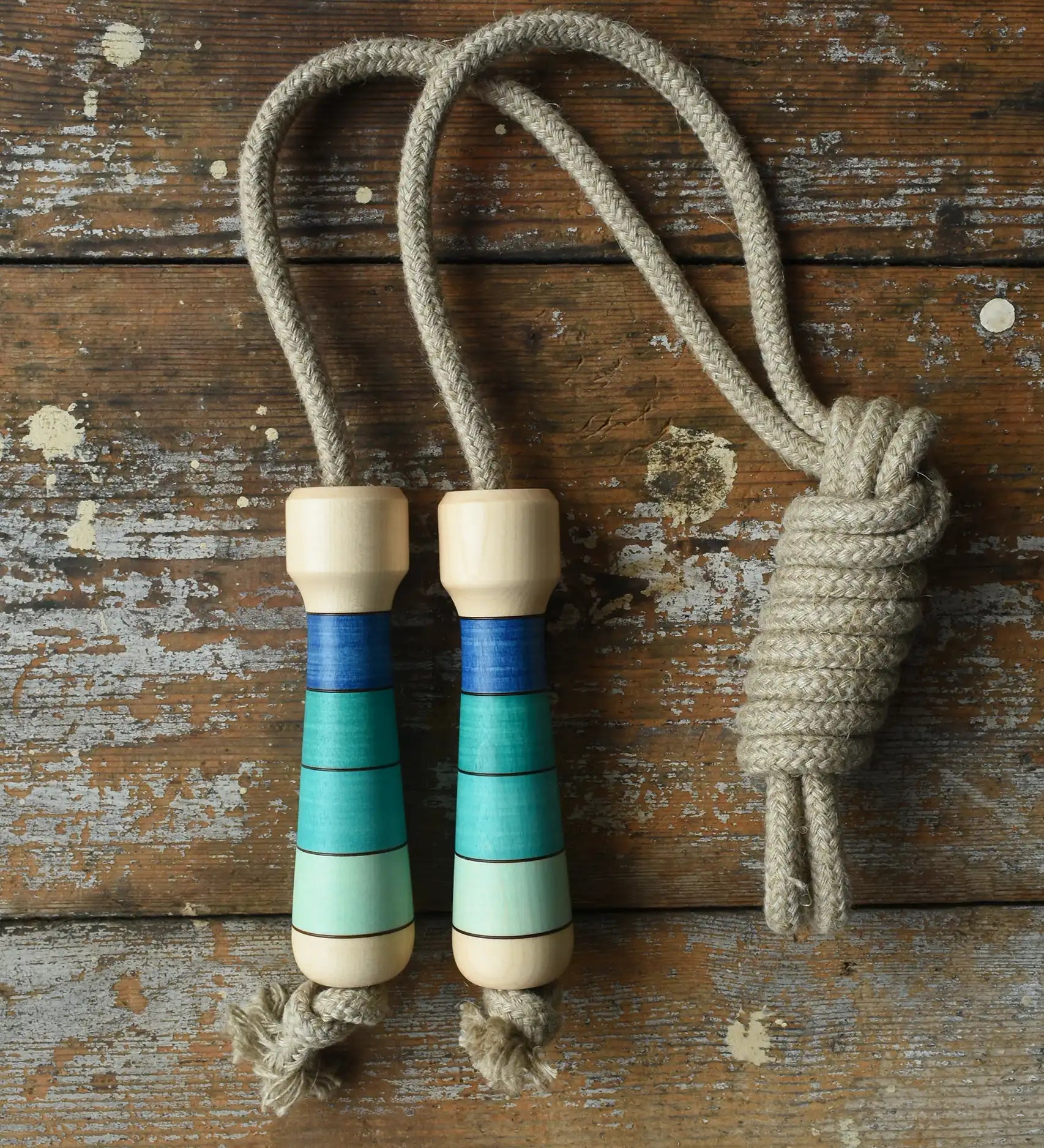 Mader Kreiselmanufaktur Skipping Rope with blue striped wooden handles placed on a wooden surface in the Babipur playroom. 