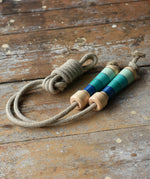 Mader Kreiselmanufaktur Skipping Rope with blue striped wooden handles placed on a wooden surface in the Babipur playroom. 