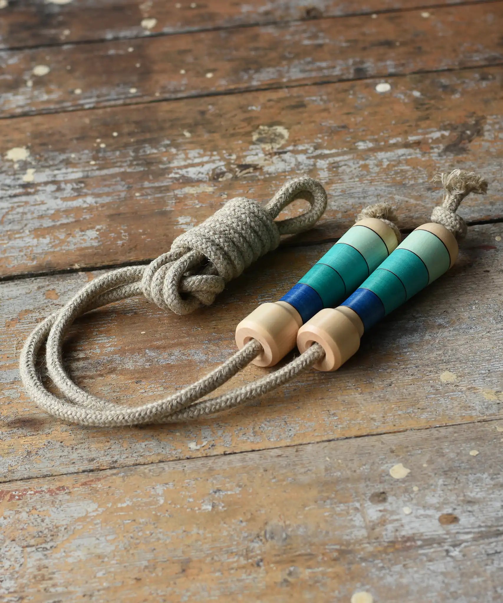 Mader Kreiselmanufaktur Skipping Rope with blue striped wooden handles placed on a wooden surface in the Babipur playroom. 