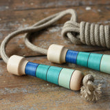 Mader Kreiselmanufaktur Skipping Rope with blue striped wooden handles placed on a wooden surface in the Babipur playroom. 