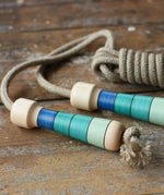 Mader Kreiselmanufaktur Skipping Rope with blue striped wooden handles placed on a wooden surface in the Babipur playroom. 