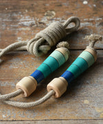 Mader Kreiselmanufaktur Skipping Rope with blue striped wooden handles placed on a wooden surface in the Babipur playroom. 