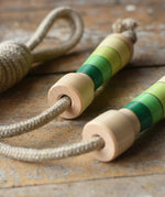Mader Kreiselmanufaktur Skipping Rope with green striped wooden handles placed on a wooden board in the Bbaipur playroom.