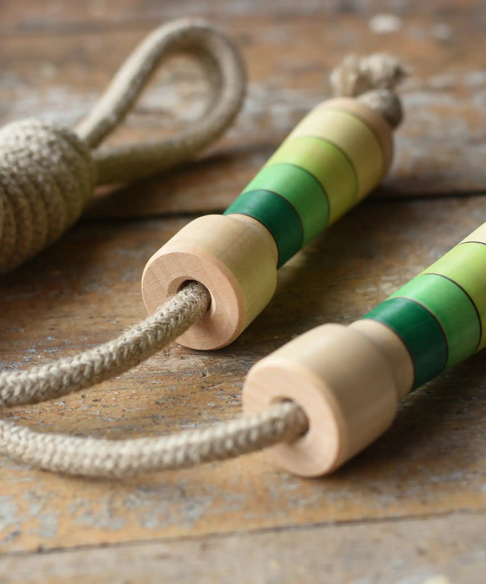 Mader Kreiselmanufaktur Skipping Rope with green striped wooden handles placed on a wooden board in the Bbaipur playroom.