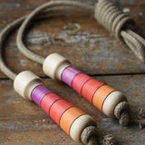 Mader Kreiselmanufaktur Skipping Rope with pink red striped wooden handles placed on a wooden surface in the Babipur playroom. 