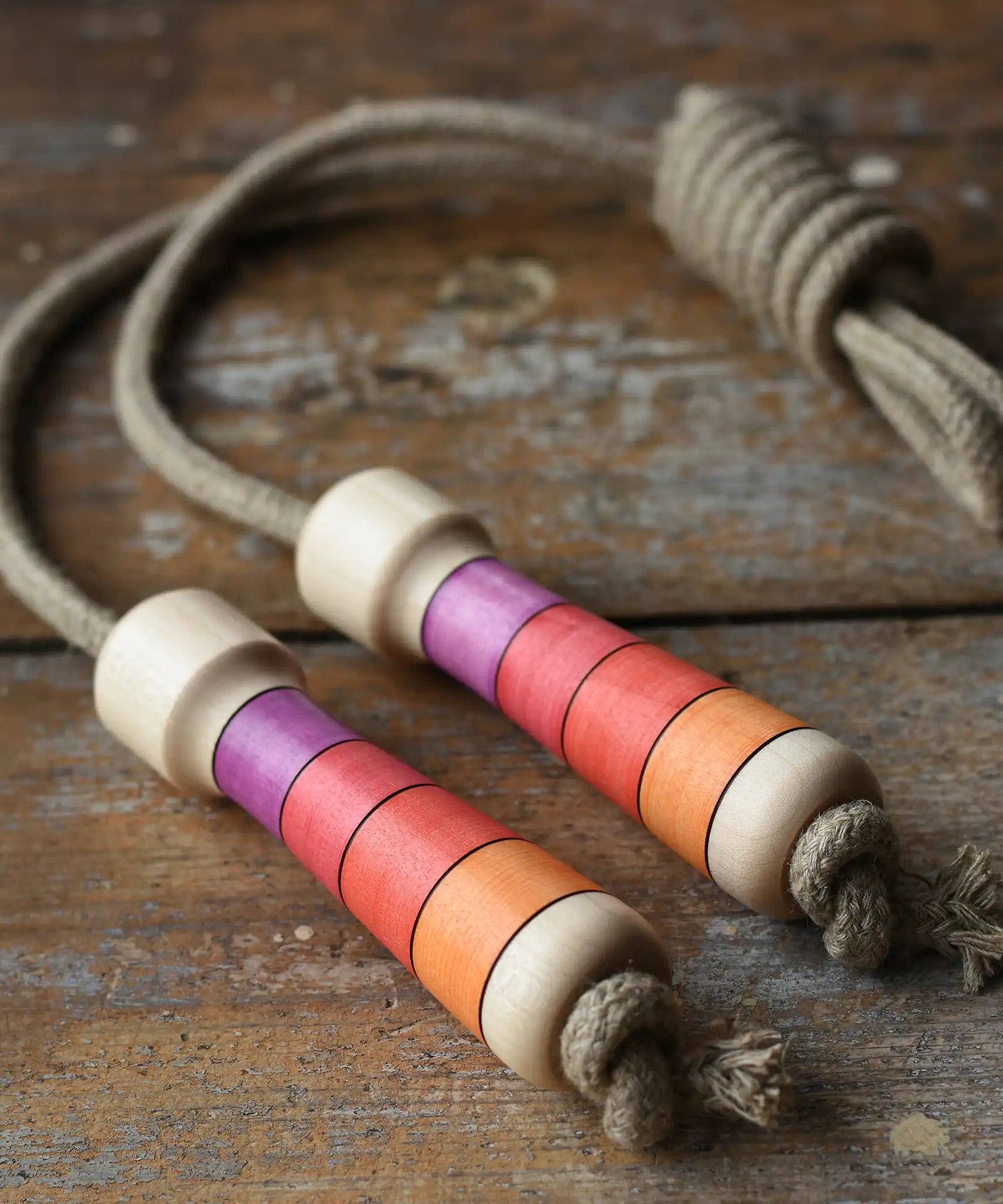 Mader Kreiselmanufaktur Skipping Rope with pink red striped wooden handles placed on a wooden surface in the Babipur playroom. 