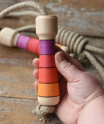 Mader Kreiselmanufaktur Skipping Rope with pink red striped wooden handles placed on a wooden surface in the Babipur playroom. 