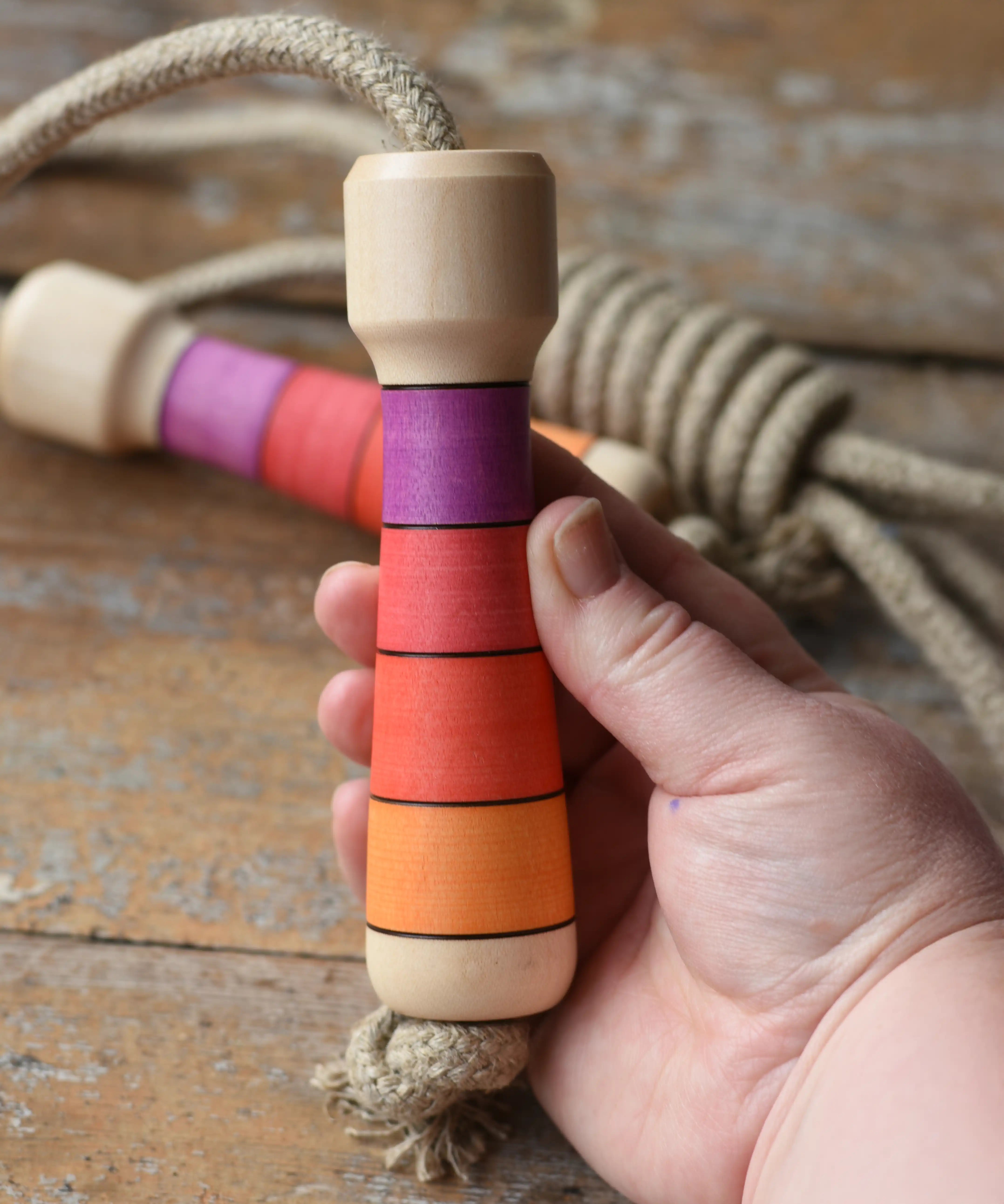Mader Kreiselmanufaktur Skipping Rope with pink red striped wooden handles placed on a wooden surface in the Babipur playroom. 