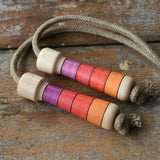 Mader Kreiselmanufaktur Skipping Rope with pink red striped wooden handles placed on a wooden surface in the Babipur playroom. 