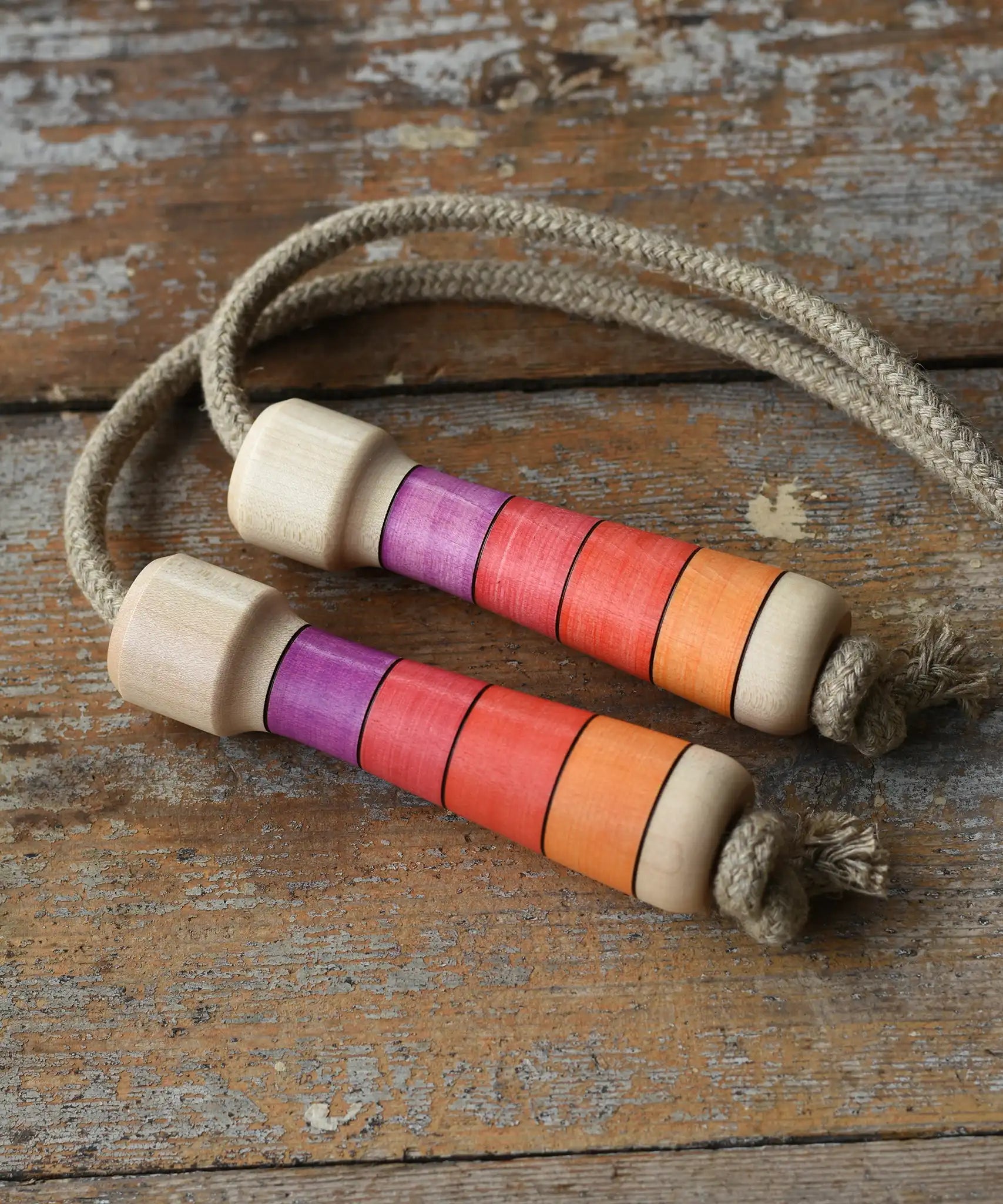 Mader Kreiselmanufaktur Skipping Rope with pink red striped wooden handles placed on a wooden surface in the Babipur playroom. 