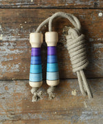 Mader Kreiselmanufaktur Skipping Rope with purple striped wooden handles placed on a wooden surface in the Babipur playroom. 