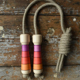 Mader Kreiselmanufaktur Skipping Rope with pink red striped wooden handles placed on a wooden surface in the Babipur playroom. 