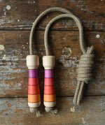 Mader Kreiselmanufaktur Skipping Rope with pink red striped wooden handles placed on a wooden surface in the Babipur playroom. 