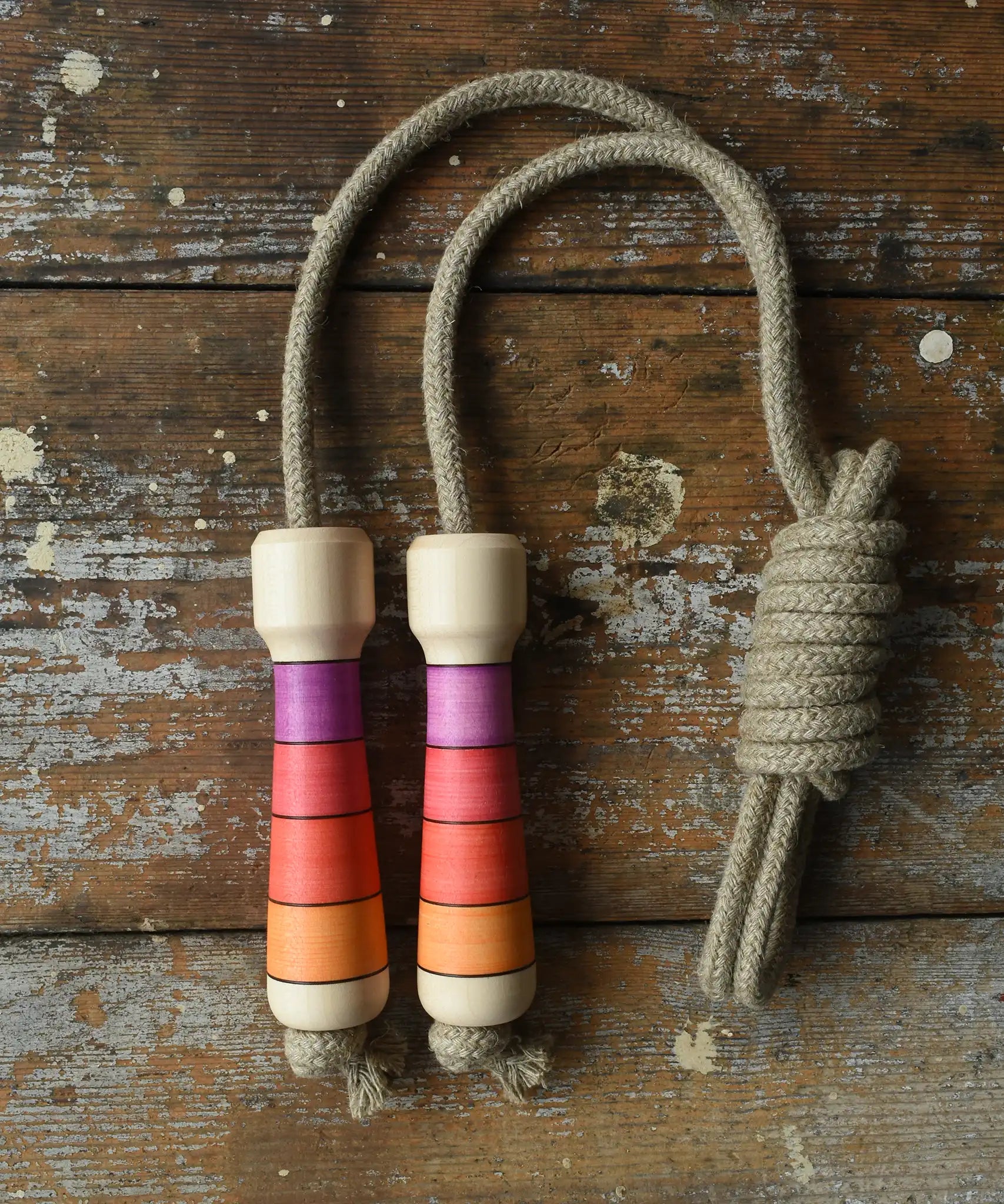 Mader Kreiselmanufaktur Skipping Rope with pink red striped wooden handles placed on a wooden surface in the Babipur playroom. 