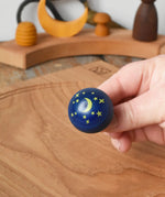 Close up of the stars and moon design on the Luna turn over top spinner, shown in an adult's hand in the Babipur playroom.