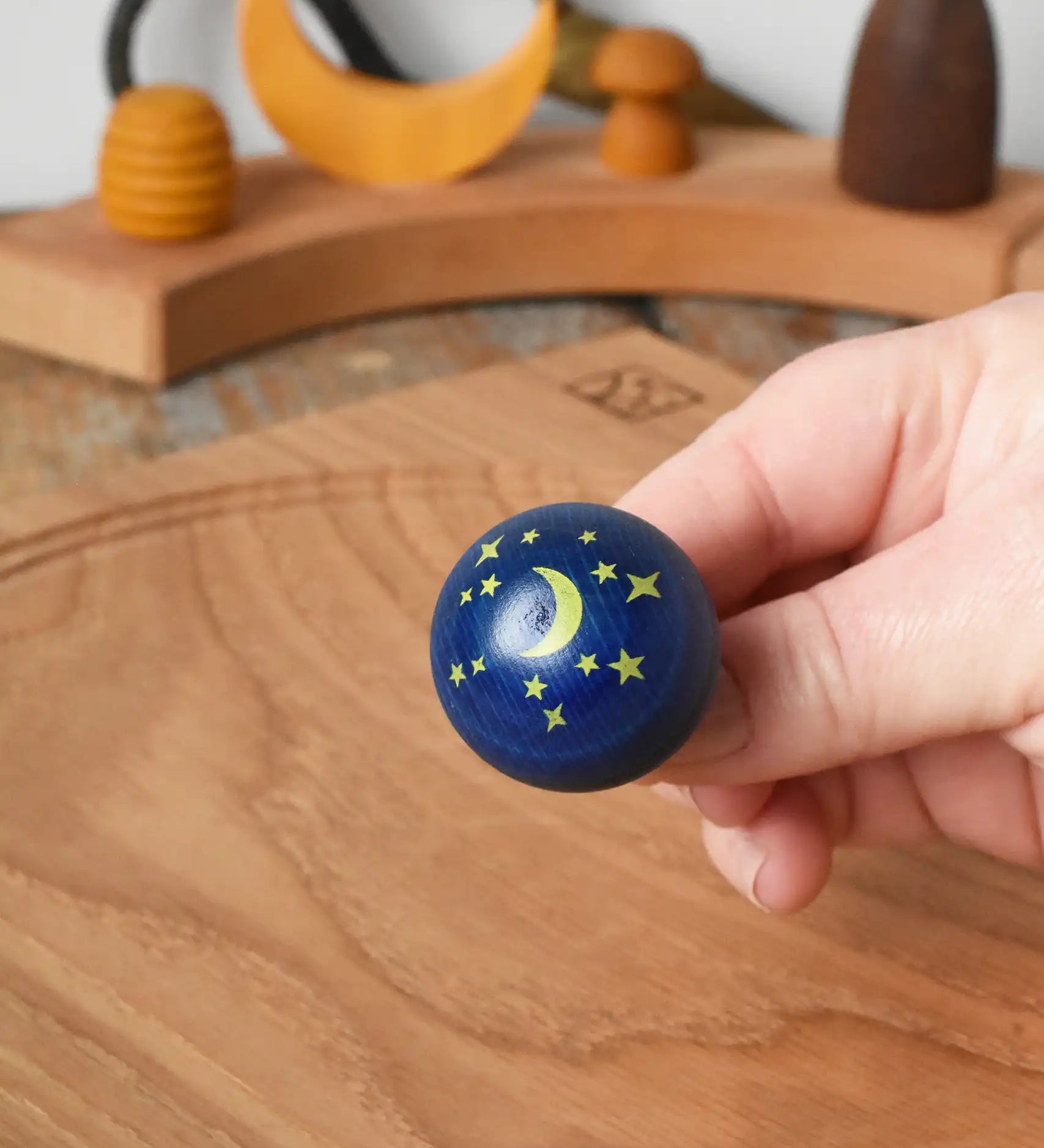 Close up of the stars and moon design on the Luna turn over top spinner, shown in an adult's hand in the Babipur playroom.
