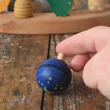 Mader Luna turn over spinning top shown on a wooden desk in the Babipur playroom. An adult's hand is holding it on a slant.
