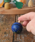 Mader Luna turn over spinning top shown on a wooden desk in the Babipur playroom. An adult's hand is holding it on a slant.