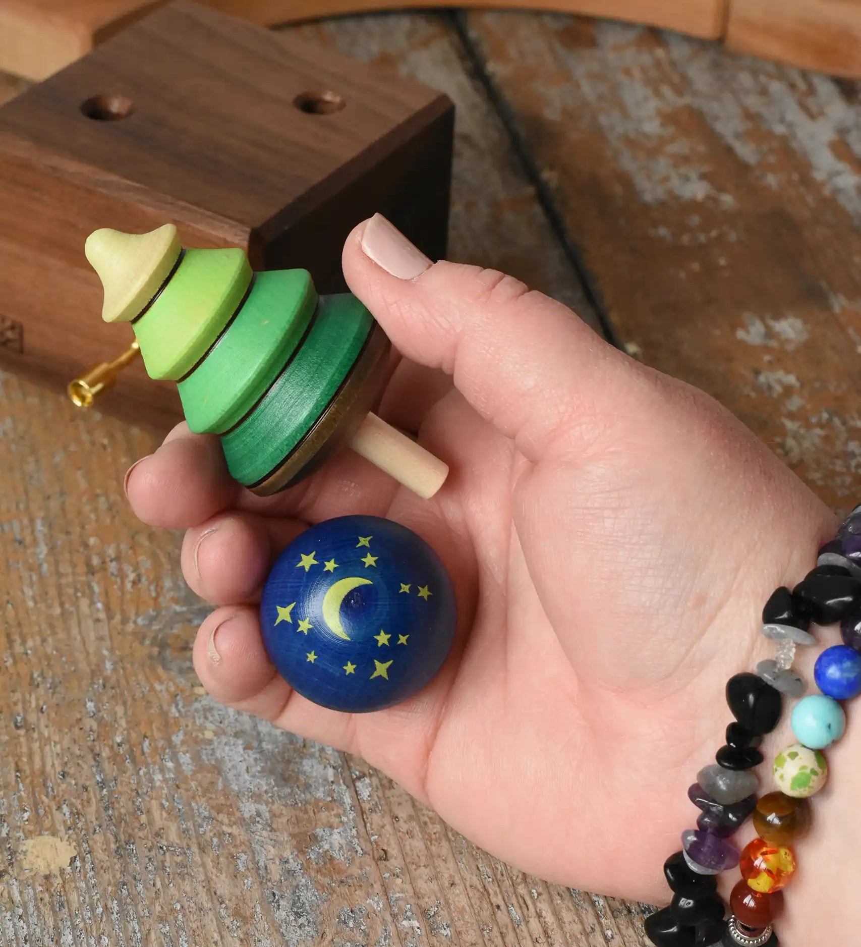Green tree shaped spinner and luna turn over spinning to from the Mader Kreiselmanufaktur luna music box shown in an adult's hand in the Babipur playroom. 