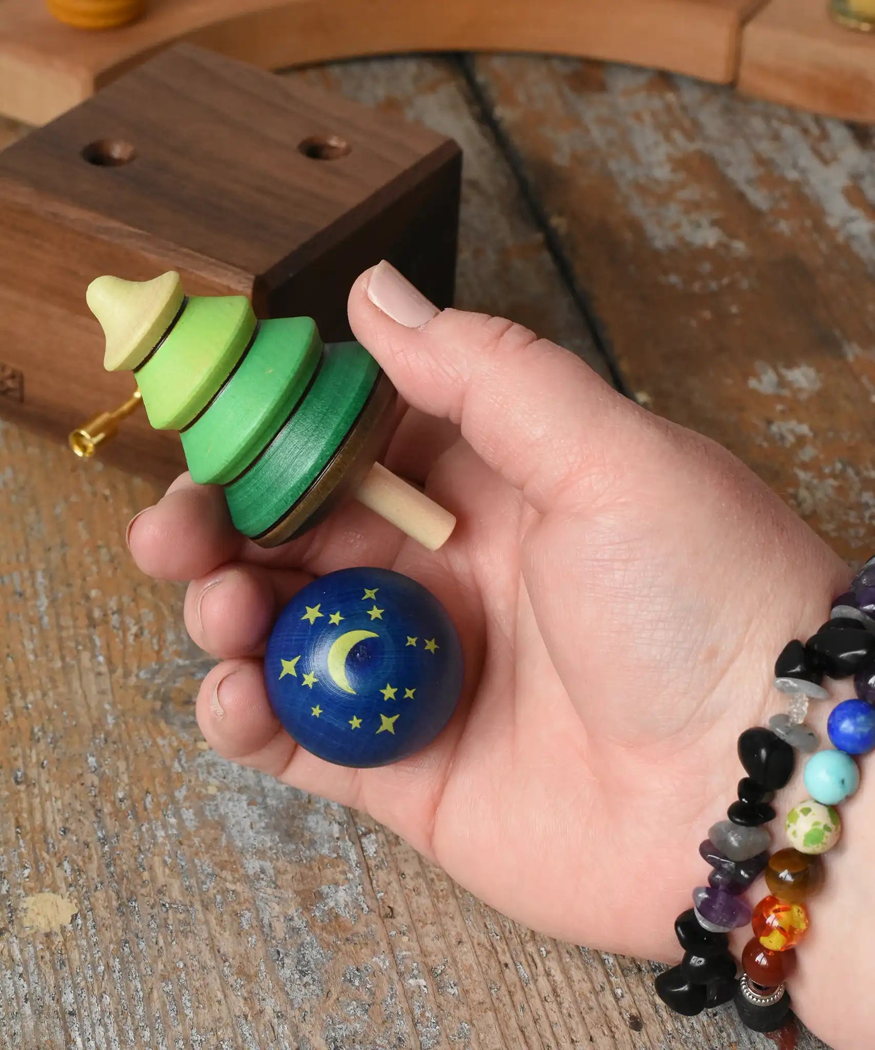 Green tree shaped spinner and luna turn over spinning to from the Mader Kreiselmanufaktur luna music box shown in an adult's hand in the Babipur playroom. 