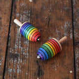 Two Mader handcrafted wooden rainbow mini thunderbolt spinning tops placed on a wooden surface in the Babipur playroom.