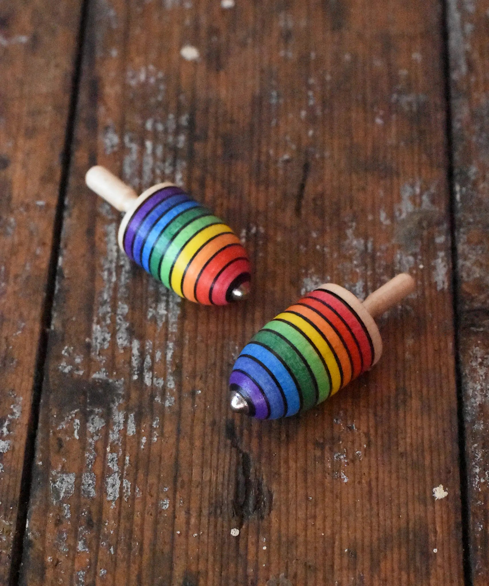 Two Mader handcrafted wooden rainbow mini thunderbolt spinning tops placed on a wooden surface in the Babipur playroom.