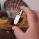 Mader handcrafted wooden rainbow mini thunderbolt spinning top in an adult's hand showing the magnet on the back.