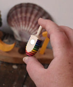 Mader handcrafted wooden rainbow mini thunderbolt spinning top in an adult's hand showing the magnet on the back.