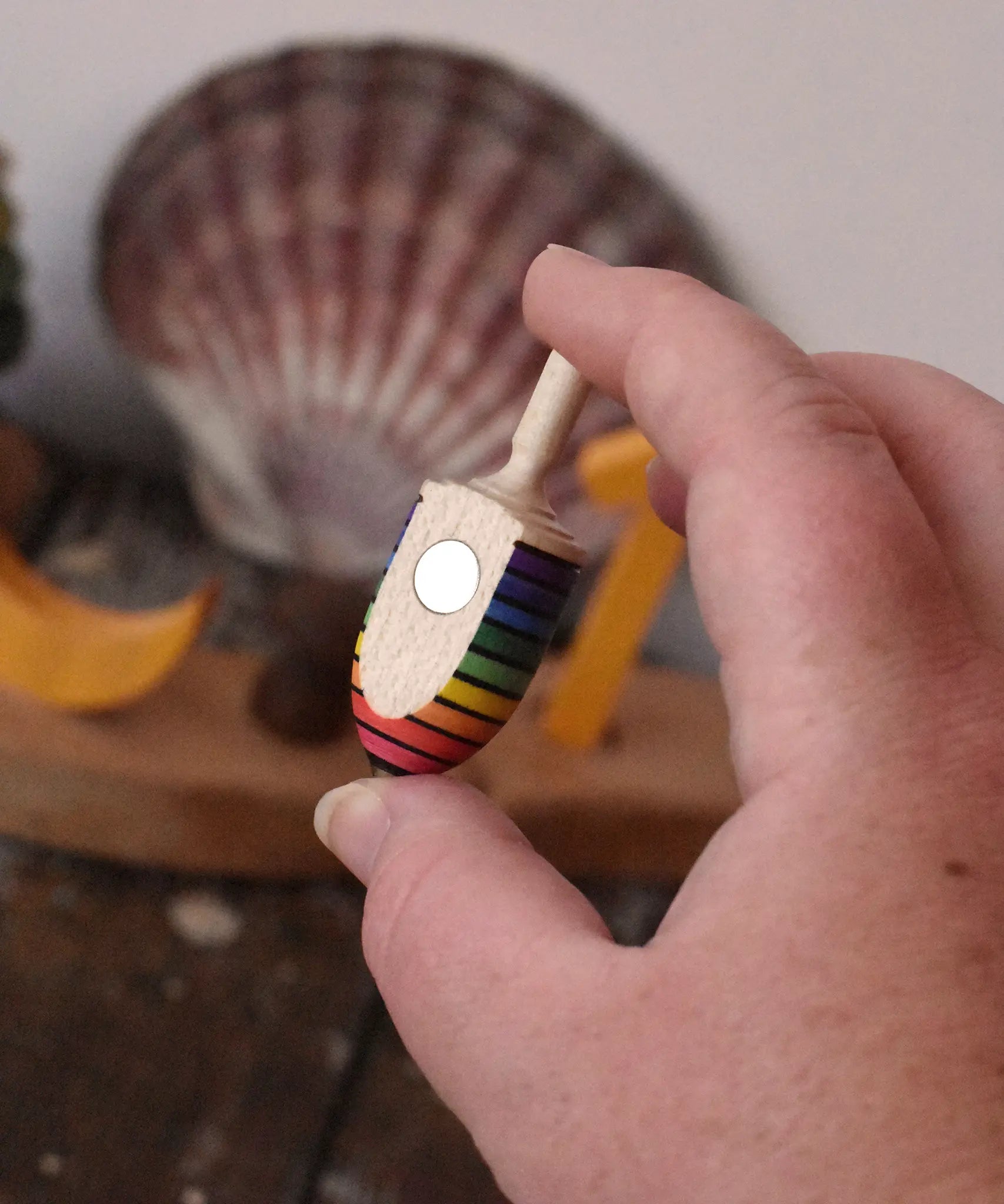 Mader handcrafted wooden rainbow mini thunderbolt spinning top in an adult's hand showing the magnet on the back.