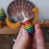 Mader handcrafted wooden rainbow mini thunderbolt spinning top in an adult's hand with a decorated Grimm's celebration ring in the background.
