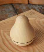 Mader Kreiselmanufaktur maple wood roly-poly pear wooden toy placed on an ash spinning plate on a wooden surface in the Babipur playroom. 