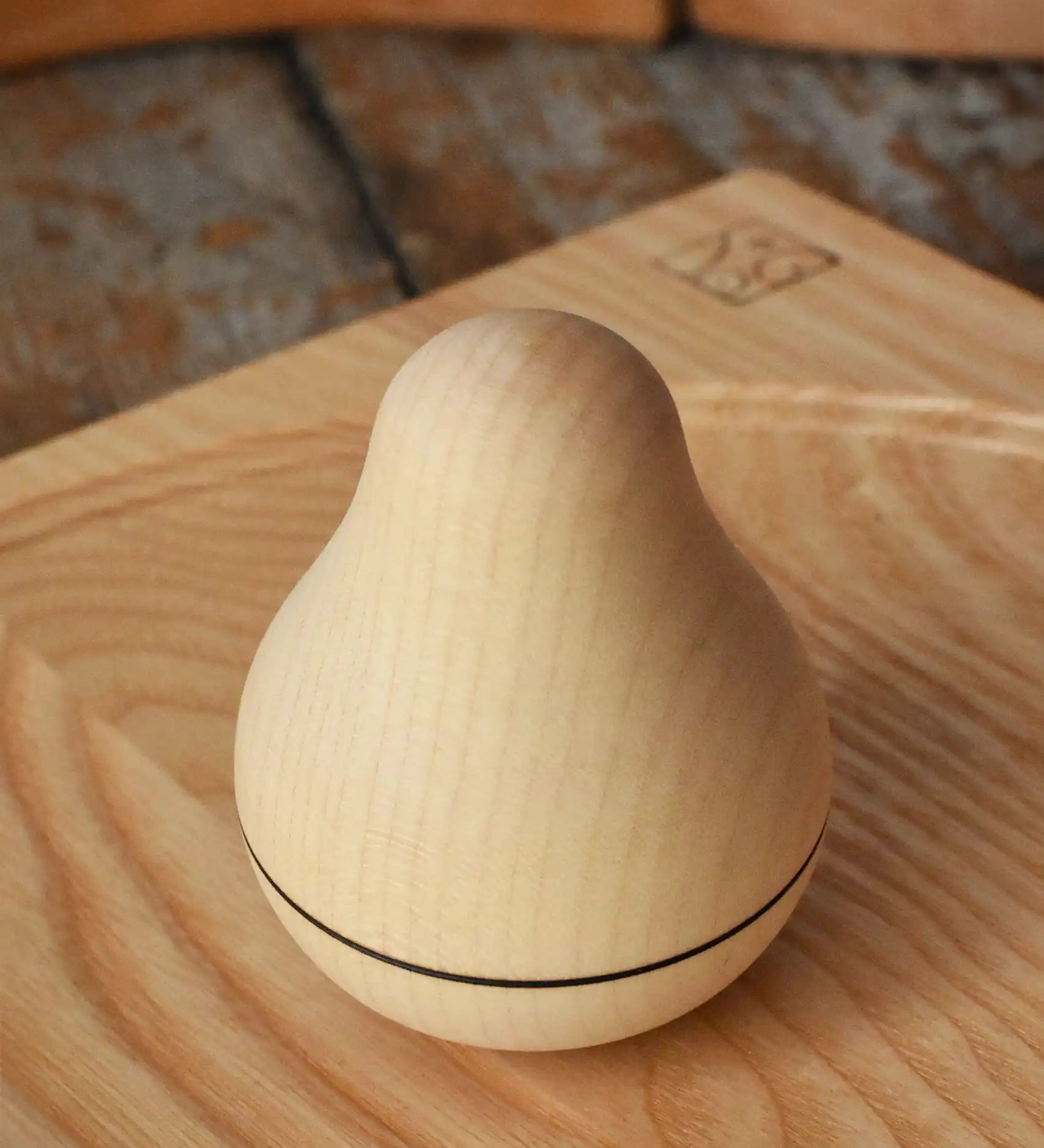 Mader Kreiselmanufaktur maple wood roly-poly pear wooden toy placed on an ash spinning plate on a wooden surface in the Babipur playroom. 