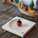 Mader maple medium wooden spinning plate 15cm placed on a wooden surface in the Babipur playroom with a red turn over spinning top.