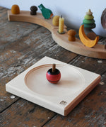 Mader maple medium wooden spinning plate 15cm placed on a wooden surface in the Babipur playroom with a red turn over spinning top.