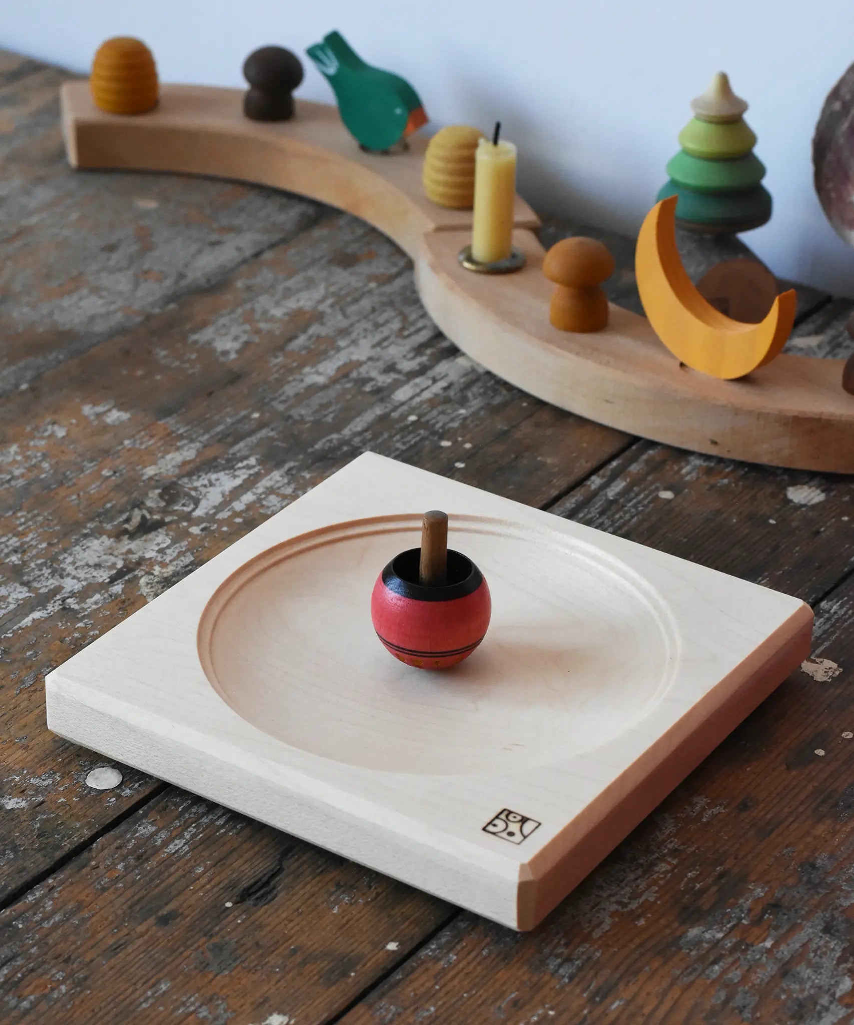 Mader maple medium wooden spinning plate 15cm placed on a wooden surface in the Babipur playroom with a red turn over spinning top.