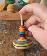 Close up of the Mader Monalotte Spinning Top on a wooden surface  help by a hand in the Babipur playroom.