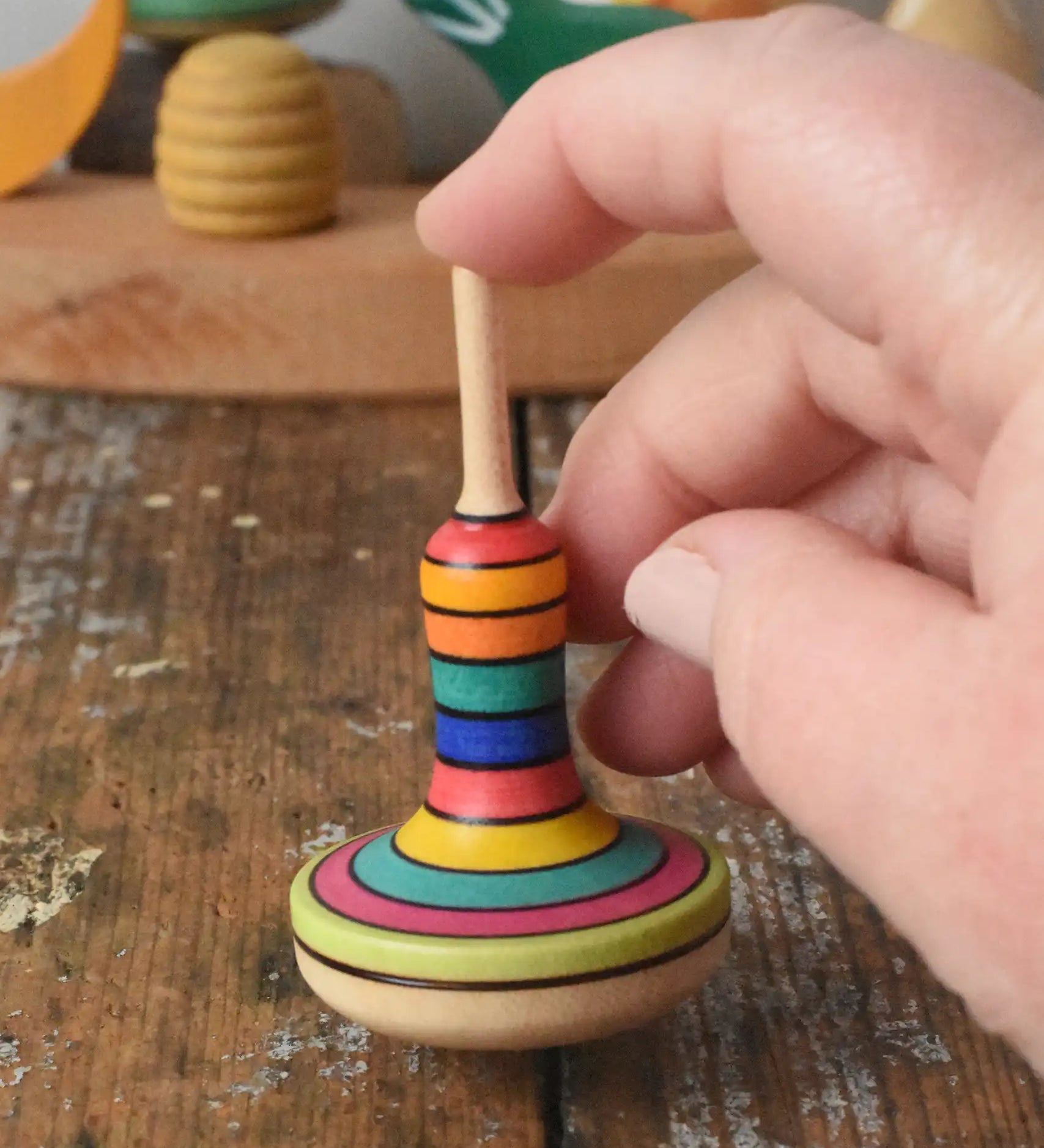 Close up of the Mader Monalotte Spinning Top on a wooden surface  help by a hand in the Babipur playroom.