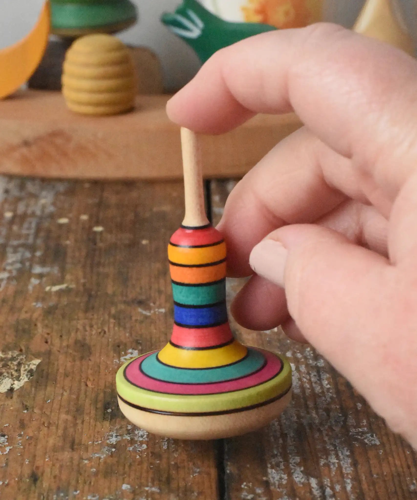 Close up of the Mader Monalotte Spinning Top on a wooden surface  help by a hand in the Babipur playroom.