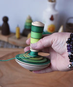 Mader wooden my first spinning top toy with starter in greenin an adult's hand in the Babipur playroom.