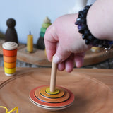Mader wooden my first spinning top toy with starter in orange being spun on a large cherry wood spinning plate   in the Babipur playroom.