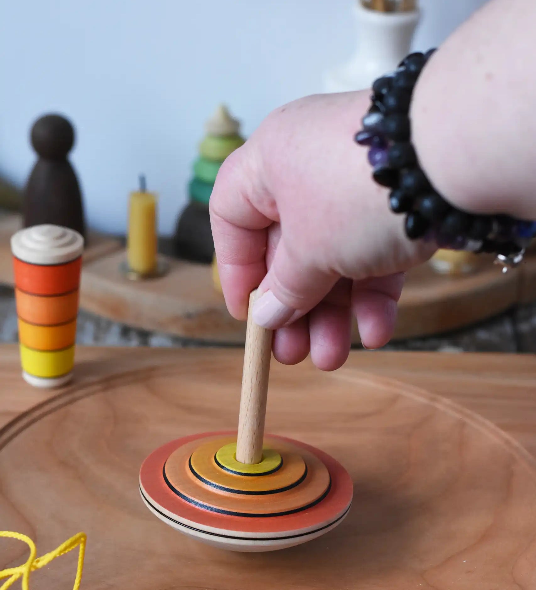 Mader wooden my first spinning top toy with starter in orange being spun on a large cherry wood spinning plate   in the Babipur playroom.