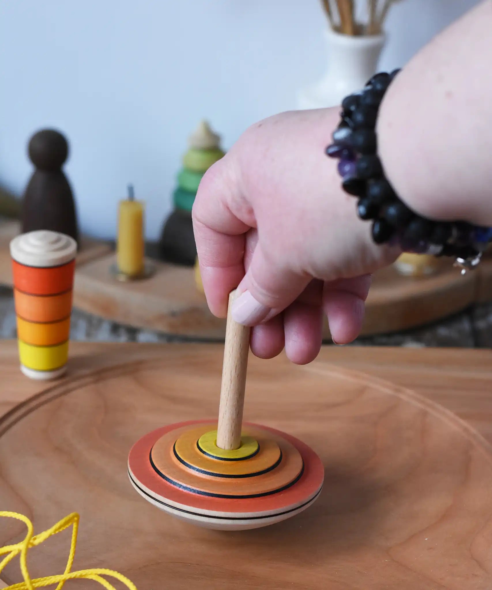 Mader wooden my first spinning top toy with starter in orange being spun on a large cherry wood spinning plate   in the Babipur playroom.