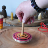 Close up of adult's hand placing the Mader wooden my first spinning top toy with starter in red on a spinning plate in the Babipur playroom.
