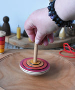 Close up of adult's hand placing the Mader wooden my first spinning top toy with starter in red on a spinning plate in the Babipur playroom.