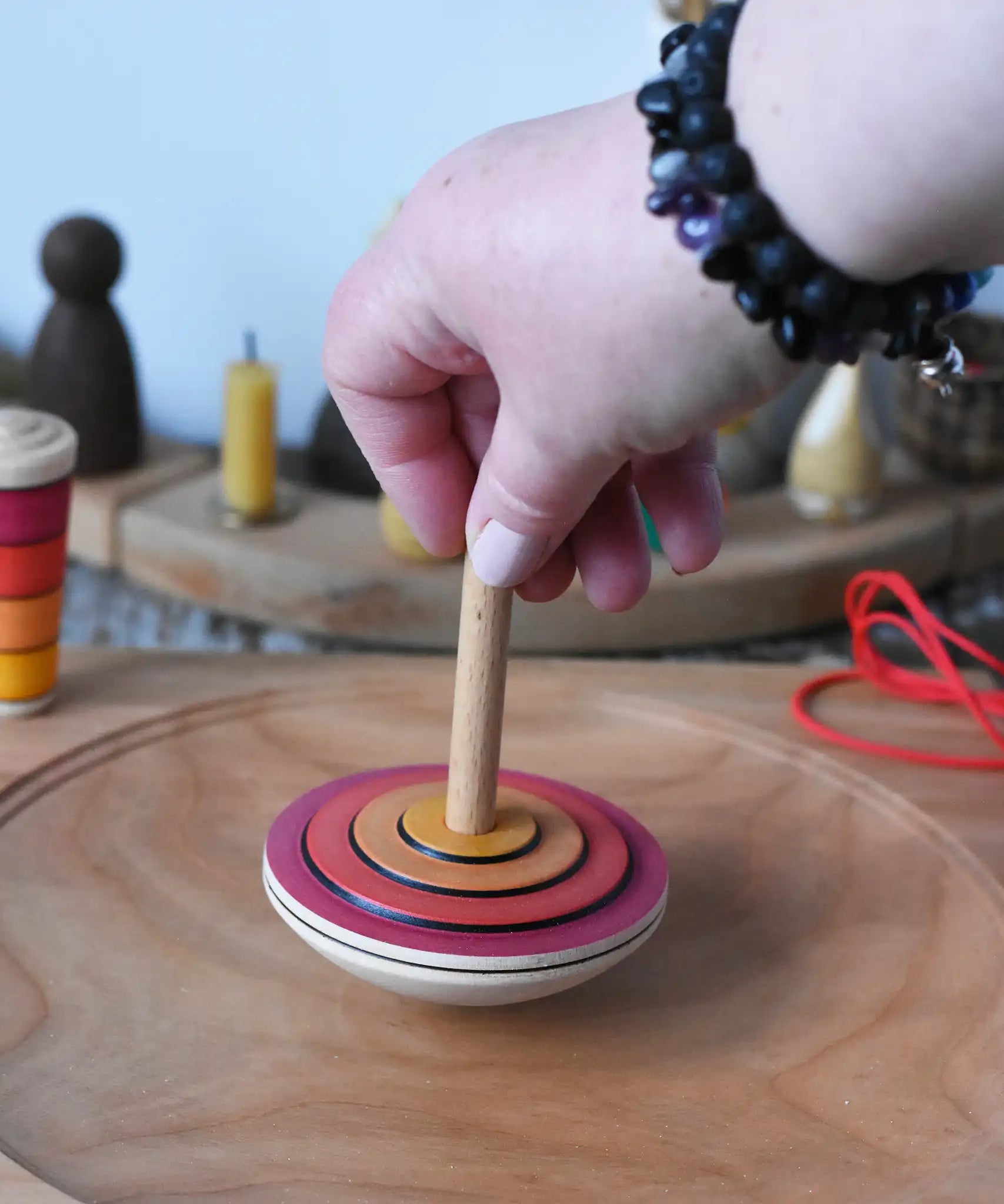 Close up of adult's hand placing the Mader wooden my first spinning top toy with starter in red on a spinning plate in the Babipur playroom.